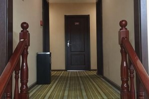 A hotel hallway with a carpeted floor, a door with a sign, and a trash bin. - Blue City Exepress Hotel (Chengdu)