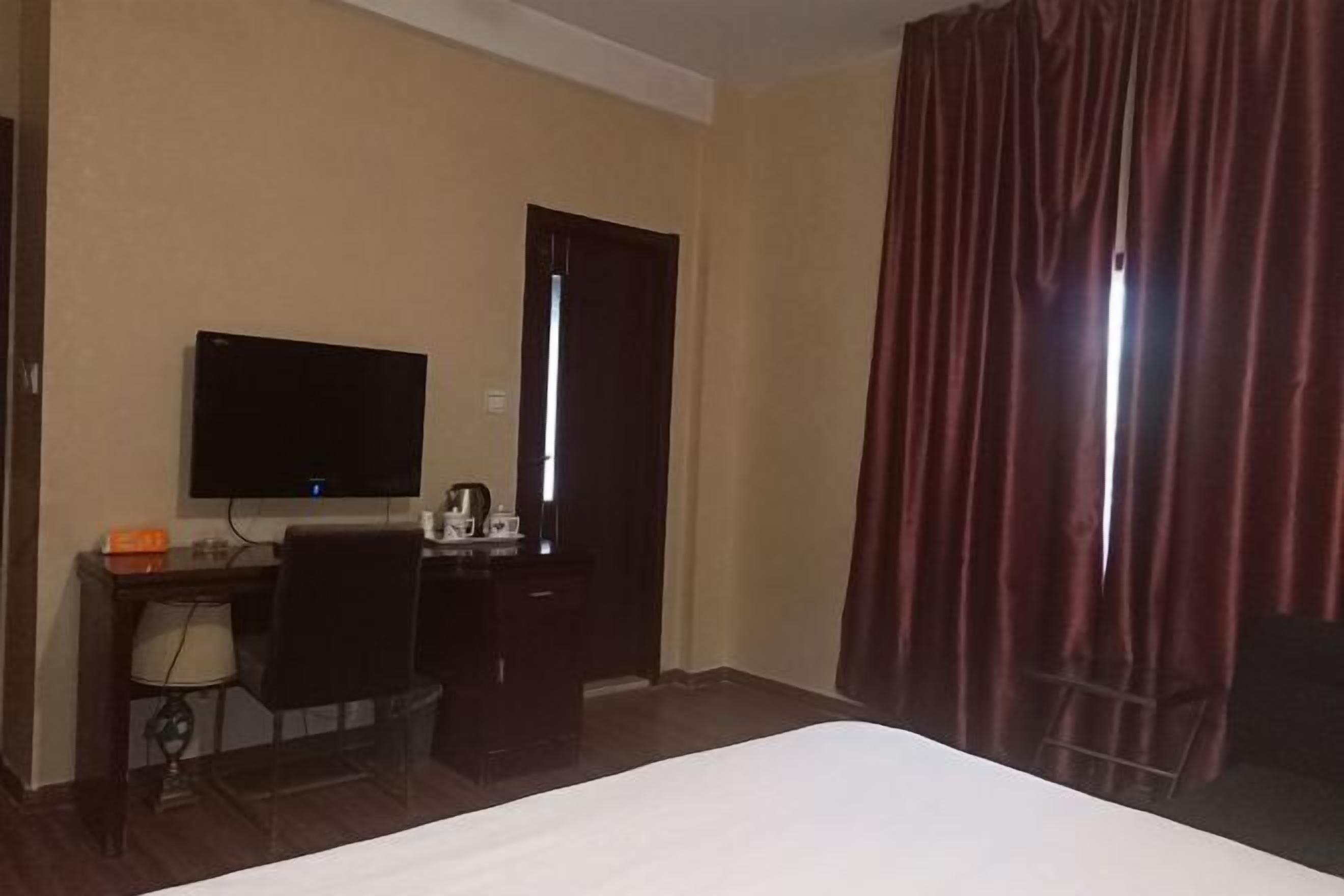 Une chambre d’hôtel comprenant un lit, un bureau avec une chaise, une télévision et une fenêtre avec des rideaux.