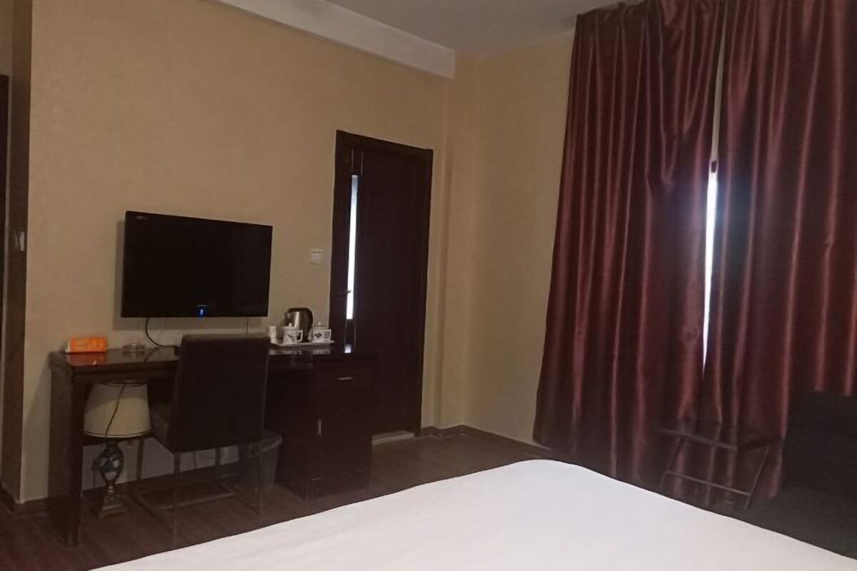 Una habitación de hotel con cama, escritorio con silla, televisor y ventana con cortinas.