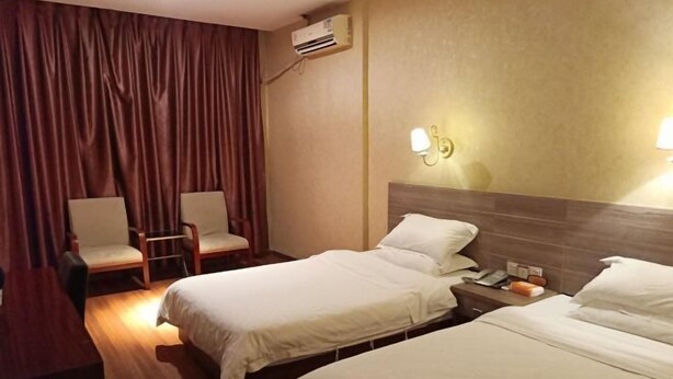 Habitación de hotel con dos camas, un escritorio, una silla, un equipo de aire acondicionado e iluminación en la pared.