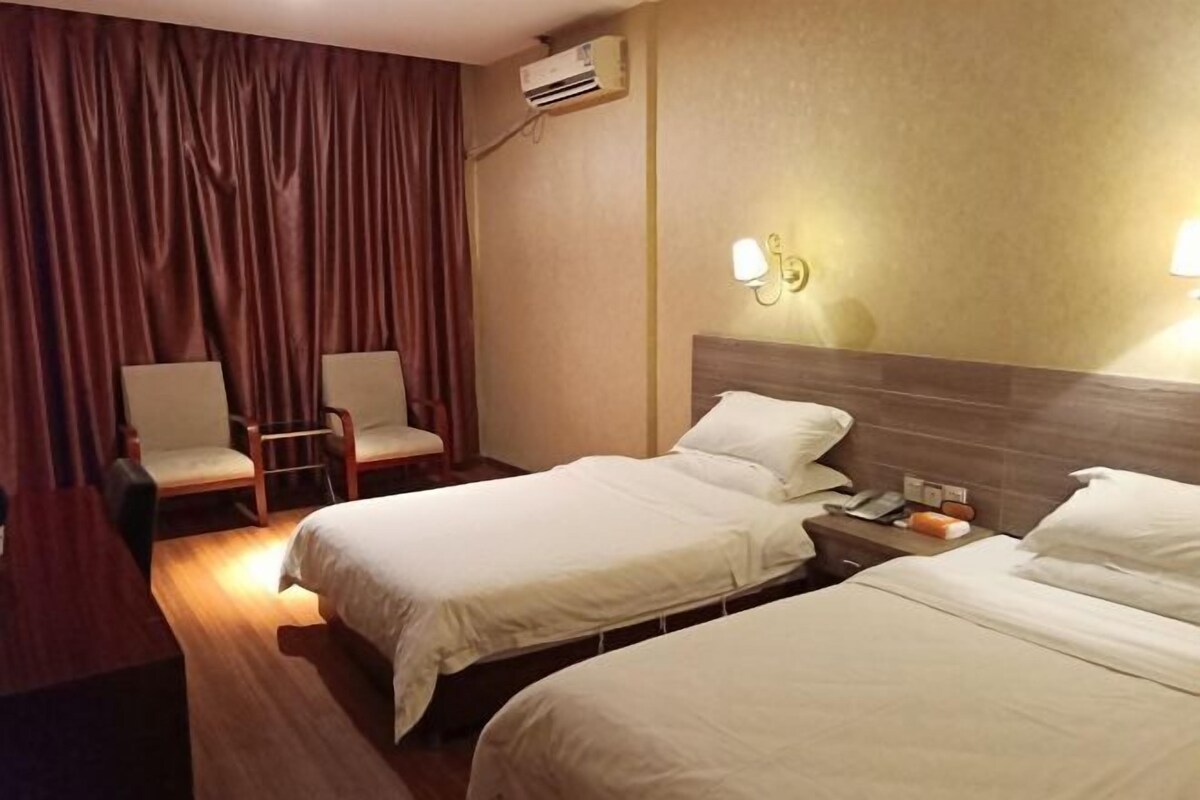 Habitación de hotel con dos camas, un escritorio, una silla, un equipo de aire acondicionado e iluminación en la pared.