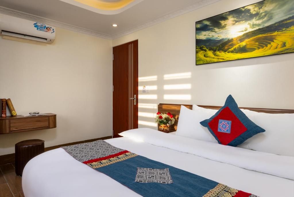 A hotel room with a large bed, a wooden nightstand, a wall-mounted air conditioner, a door, and a painting of a landscape.