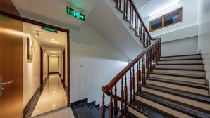 Un pasillo de hotel con piso de mármol, escalera de madera y un letrero que indica el camino a la recepción.