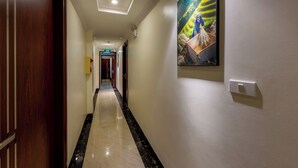 Un couloir d’hôtel avec un sol en marbre poli, une porte en bois et un tableau encadré accroché au mur.