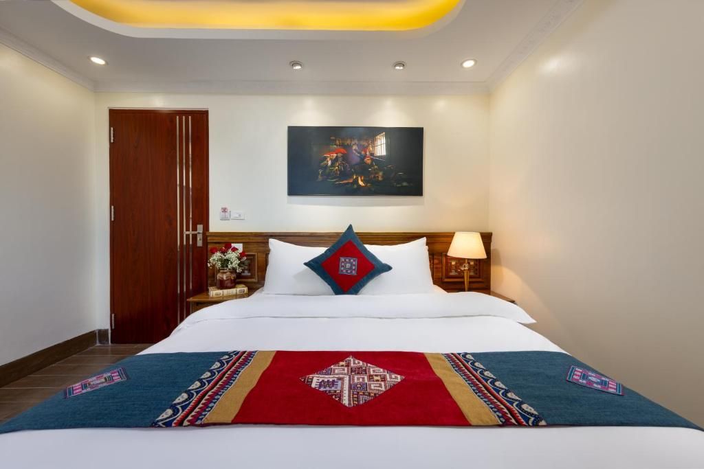 A hotel room with a bed, a nightstand, a lamp, a painting on the wall, and a wooden door.