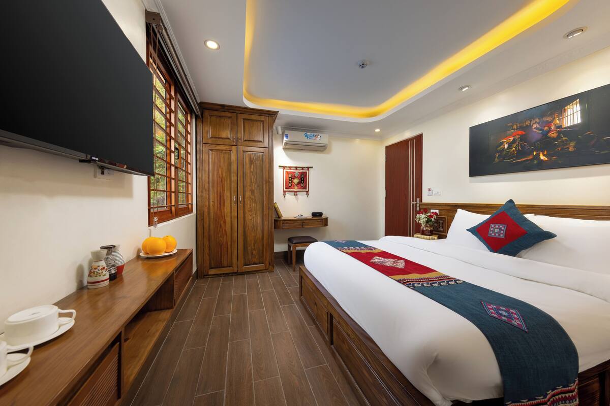 Habitación de hotel con una cama grande, armario de madera, escritorio y un cuadro en la pared.