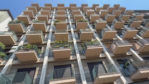 A high-rise building with multiple balconies, each with a small garden area.