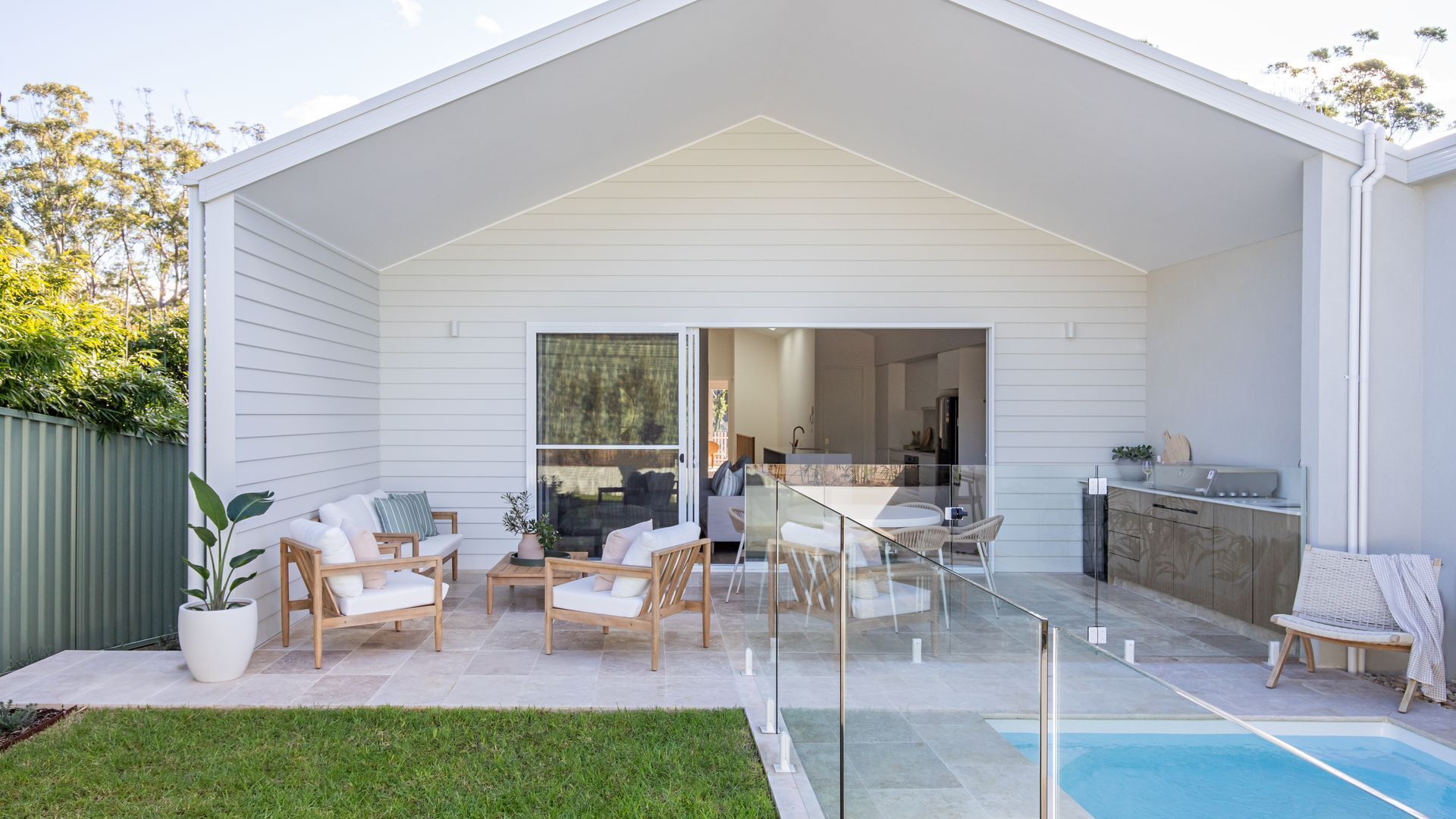 A modern house with a covered patio, a pool, and a kitchen visible through the glass doors.