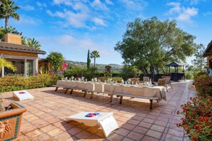 Un espace de restauration en plein air avec de longues tables dressées pour un repas, entouré d’une végétation luxuriante et sous un ciel bleu dégagé.