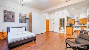 Une chambre spacieuse avec un grand lit, un plancher en bois et une cuisine moderne située dans la pièce adjacente.