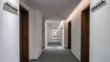 Pasillo de hotel con puertas numeradas 60703 y 60706, piso alfombrado y una lámpara moderna.