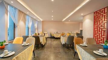 Un comedor de hotel con mesas preparadas para los huéspedes, ventanas amplias con cortinas y un diseño decorativo en la pared.