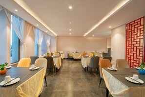 A hotel dining area with tables set for guests, large windows with curtains, and a decorative wall pattern. - Bo Man Hotel (Pu'er)