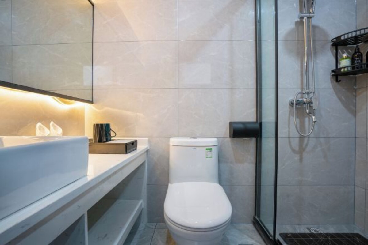 A modern bathroom with a white toilet, a glass shower enclosure, and a white sink with a mirror above it.