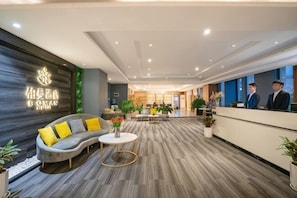 A hotel lobby with a reception desk, sofas, a coffee table, and potted plants.