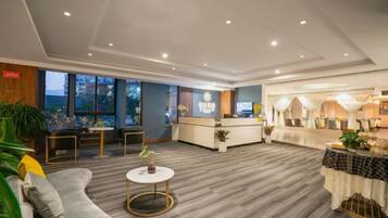 A hotel lobby with a reception desk, seating area, and a dining space.