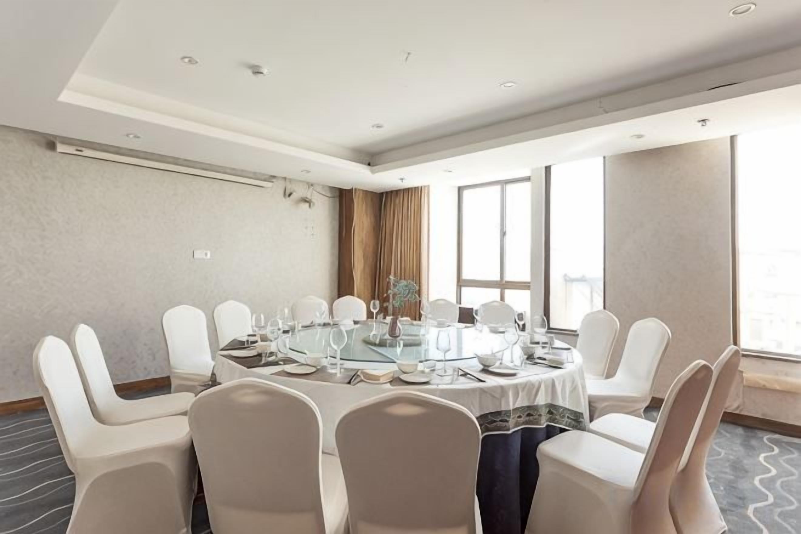 Una sala de conferències amb una taula rodona, caires blancs i una finestra amb cortines.