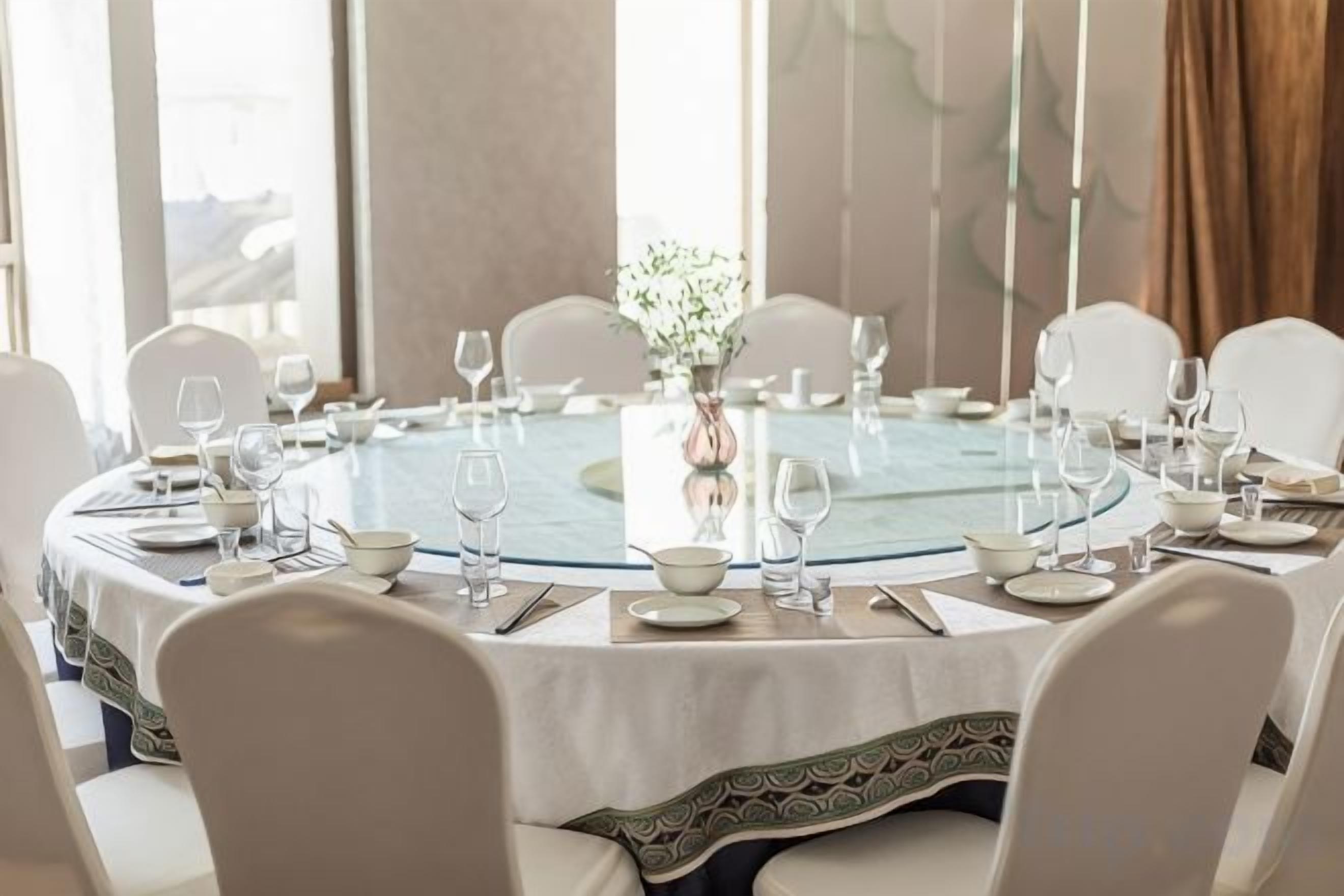 Une table de salle à manger ronde, entourée de chaises blanches, mise avec des assiettes, des verres et un vase rempli de fleurs.