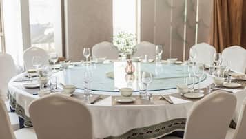Une table de salle à manger ronde, entourée de chaises blanches, mise avec des assiettes, des verres et un vase rempli de fleurs.