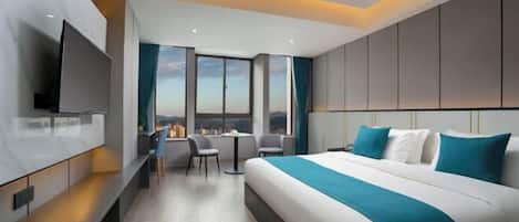 A modern hotel room with a large bed, a TV, a desk with chairs, and a view of the city.