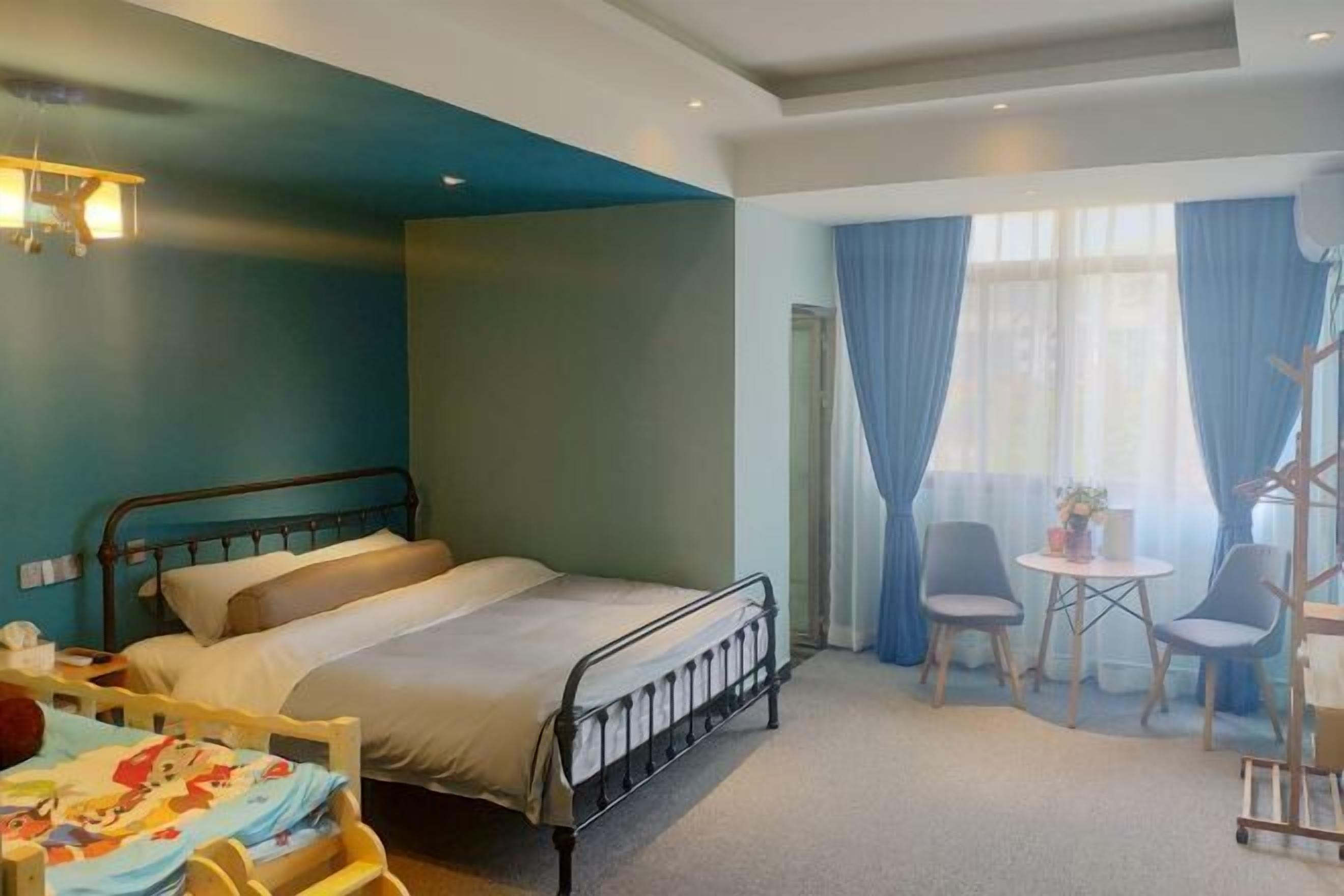 A hotel room with a bed, a desk, two chairs, and a small table with a lamp.