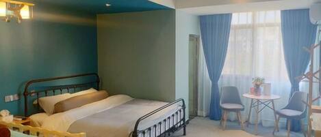 A hotel room with a bed, a desk, two chairs, and a small table with a lamp.