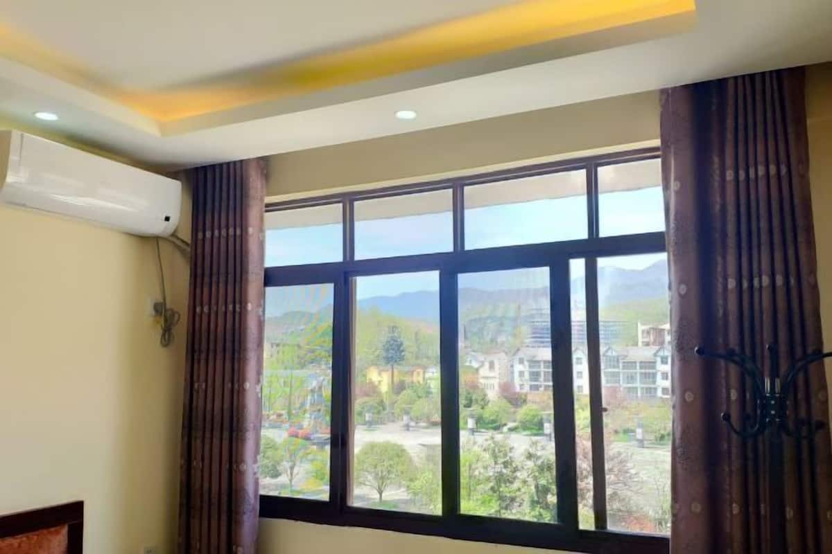A room with a large window, an air conditioning unit, and a view of a residential area.