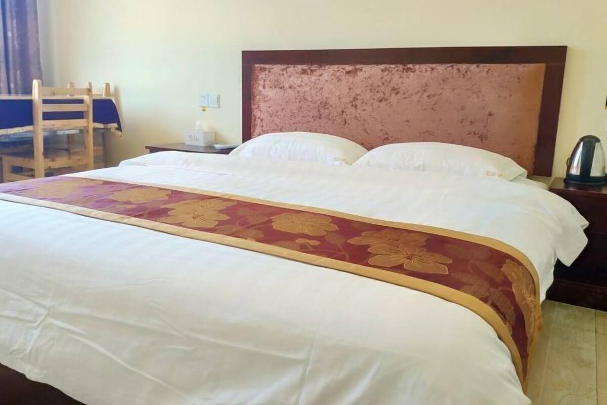 A neatly made bed with a floral bedspread, a wooden headboard, and a nightstand with a kettle.