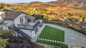 Il s’agit d’une propriété résidentielle dotée d’une pelouse bien entretenue, d’un balcon agrémenté de mobilier d’extérieur et offrant une vue sur une ville vallonnée en arrière-plan.