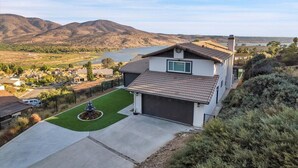 Une maison à deux étages avec un garage, une pelouse bien entretenue et une vue sur un lac et des montagnes en arrière-plan.
