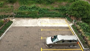 A parking area with a car, brick pavement, and a grassy hill in the background. - Yunxiu Inn (Zhangjiajie)