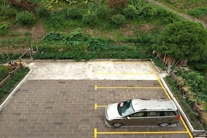 A parking area with a car, brick pavement, and a grassy hill in the background. - Yunxiu Inn (Zhangjiajie)