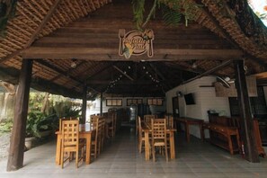 A covered outdoor dining area with wooden tables and chairs, a sign above the entrance, and a view of the surrounding greenery. - RedDoorz @ Casa Rafaelle Transient Ilocos Sur (San Vicente)