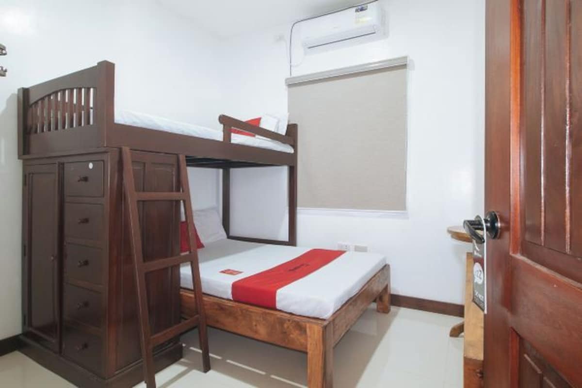 A bunk bed with a wooden ladder, a small cabinet with drawers, and a window with a blind.