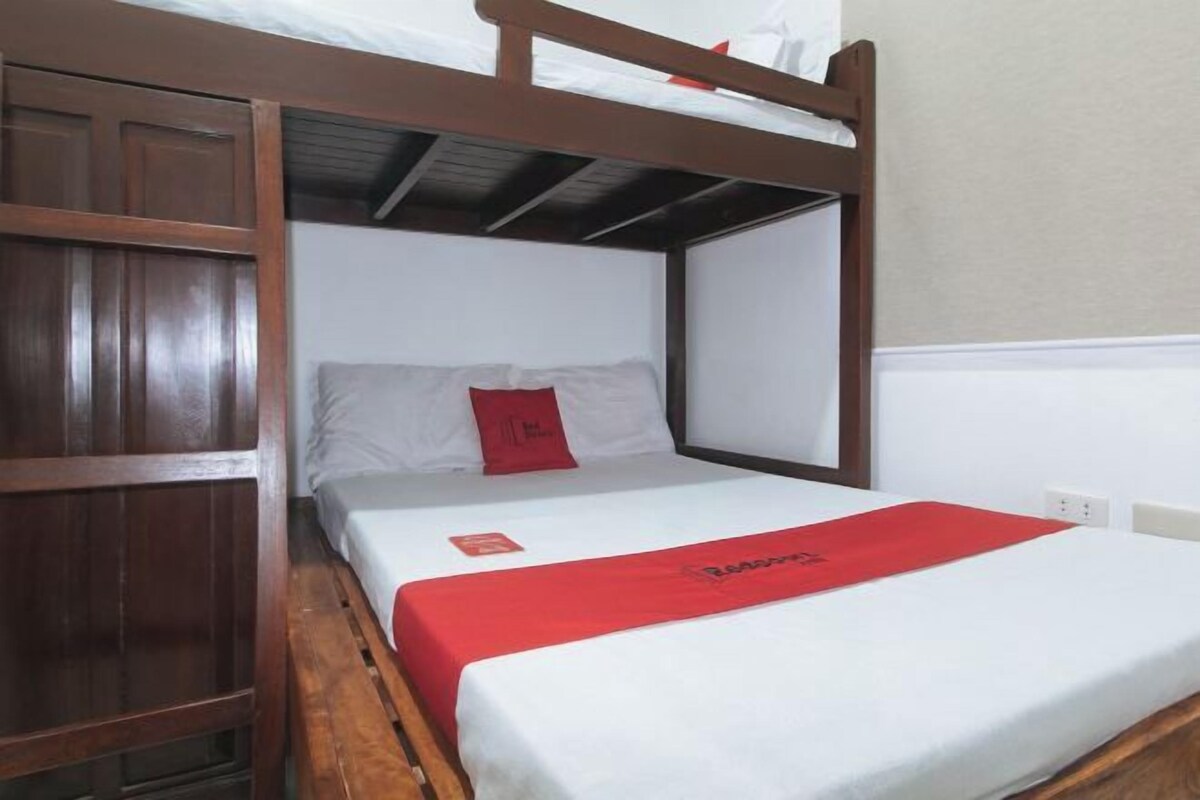 A single bed with a wooden headboard, white bedding, and a red accent pillow.