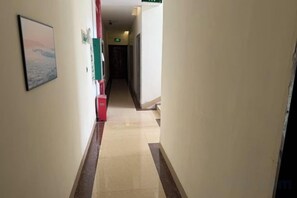 Un passadís amb un quadre al mur esquerre, un objecte vermell al mur dret i una porta al final.