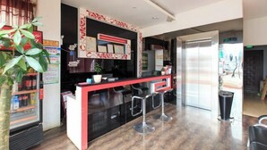 A reception area with a counter, bar stools, a refrigerator, and a potted plant. - Guests City Daren Theme Hotel (Laibin)