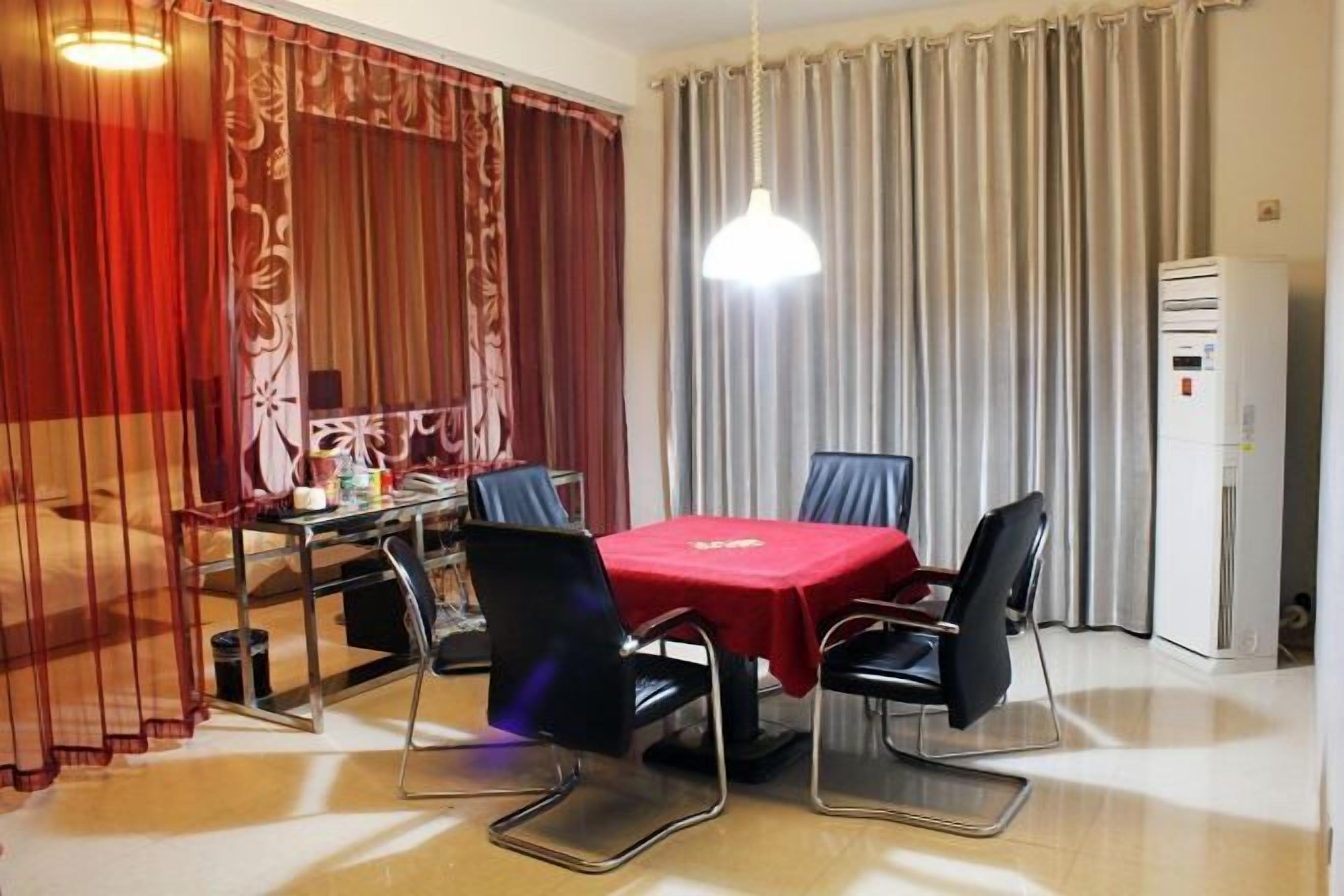 Un comedor con una mesa cubierta con mantel rojo, rodeada por cuatro sillas. Hay una lámpara en el techo sobre la mesa, y se ve un refrigerador a la derecha.