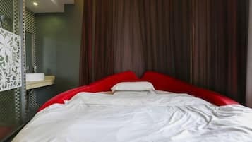 A modern hotel room with a red bed, white bedding, and a curtain backdrop.