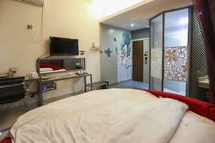 Habitación de hotel con cama, escritorio con televisor de pantalla plana, espejo y puerta corredera que da a un baño.