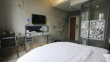 A hotel room with a bed, a desk with a flat-screen TV, a wall-mounted phone, and a decorative floral mural.