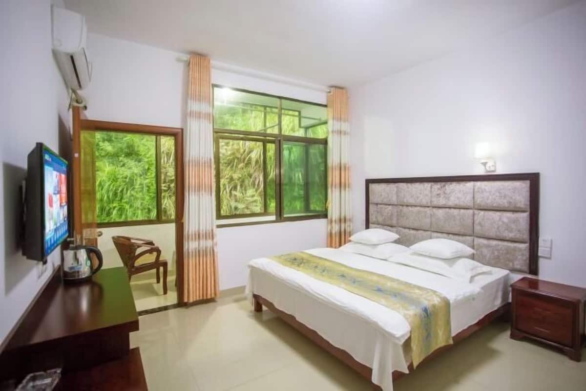 Ein Schlafzimmer mit einem Bett, einem Fernseher, einem Schreibtisch, einem Stuhl und einem Vorhangfenster.