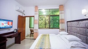 Una habitación de hotel con una cama, un escritorio con computadora, un televisor y un ventanal con cortinas.