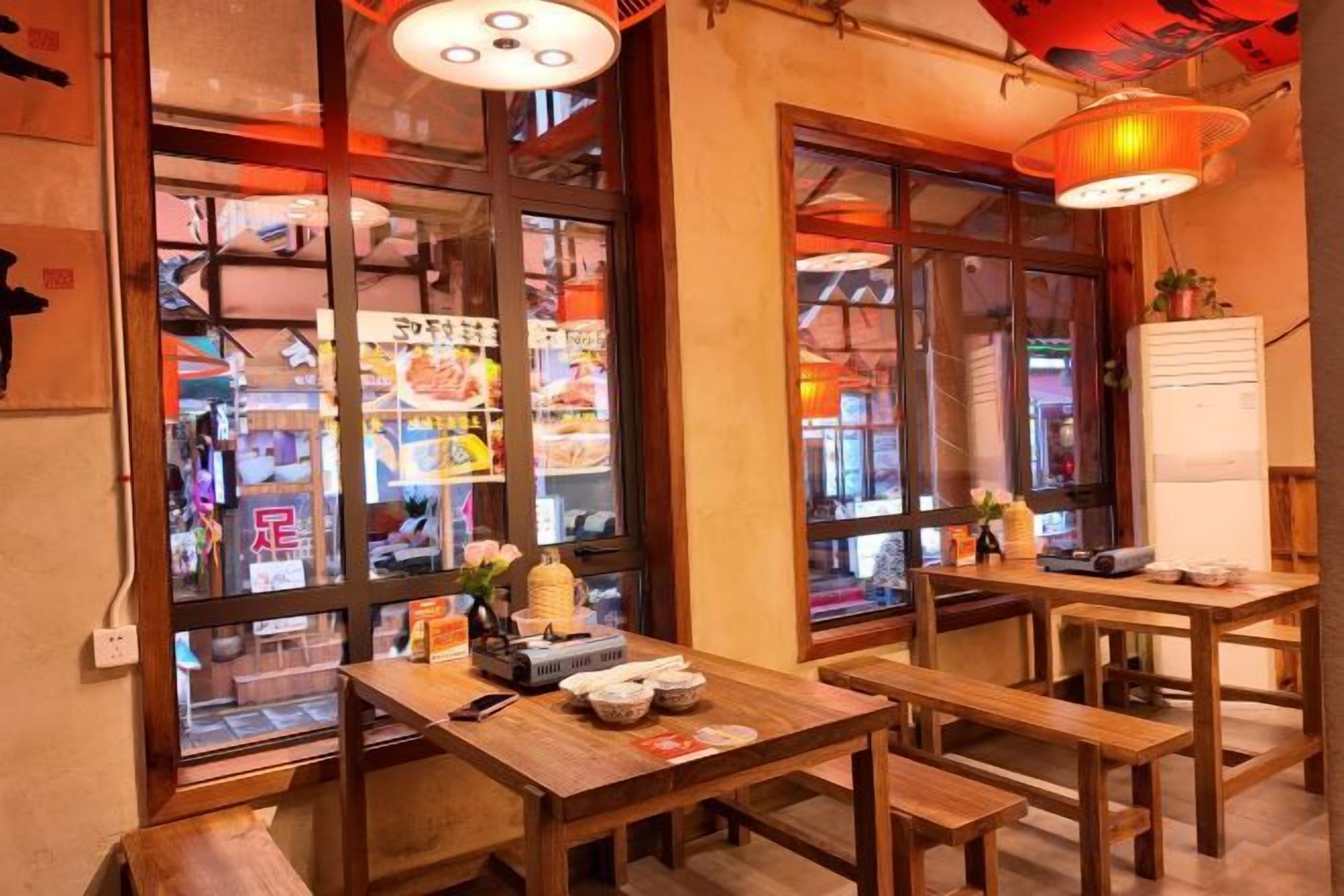 Interior de un restaurante con mesas y bancos de madera, una estética japonesa tradicional y grandes ventanales con vista a la calle.