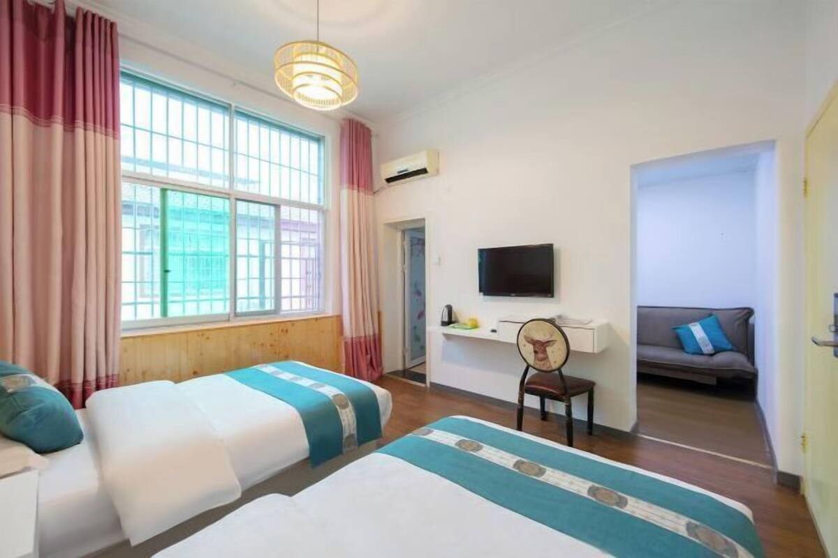 A hotel room with two beds, a TV, a desk, and a sofa.