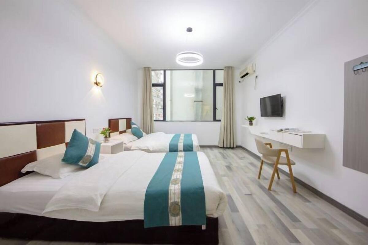 A hotel room with two beds, a desk, a TV, and a large window.