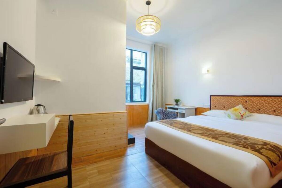 A hotel room with a bed, a desk, a chair, a TV, and a window.