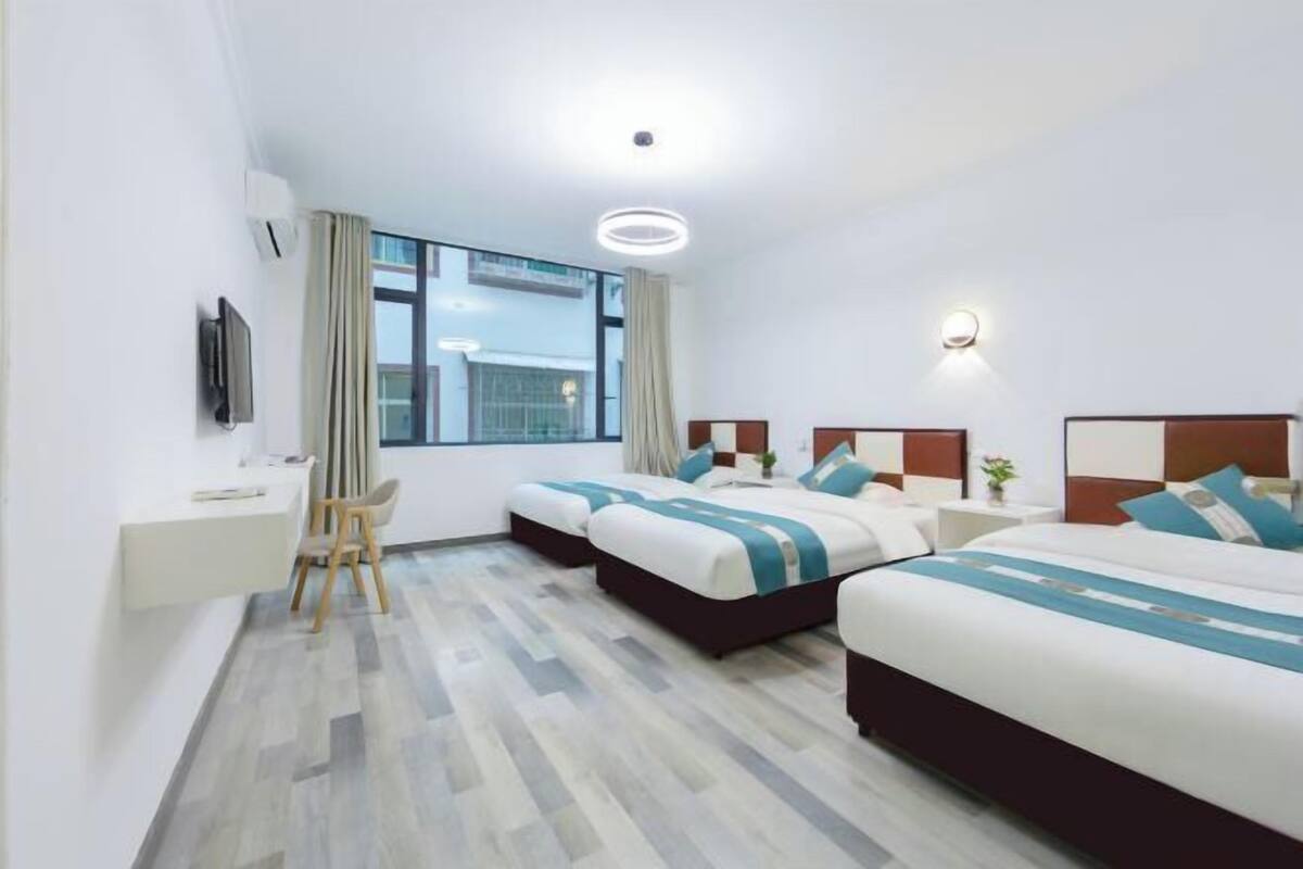 A hotel room with two beds, a desk, a chair, and a large window.