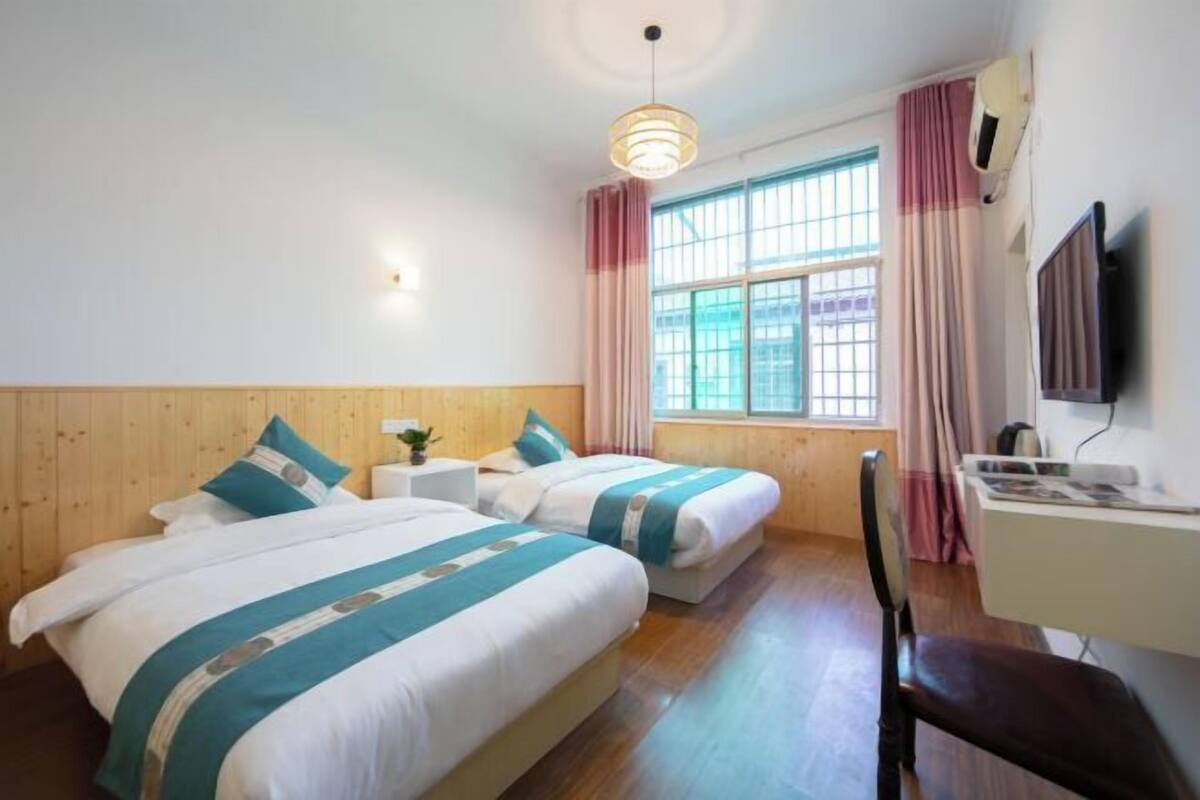 A hotel room with two beds, a desk, a chair, a television, and a window with curtains.