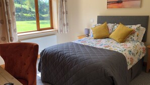 A bedroom with a bed, a chair, a nightstand, a lamp, and a window with curtains. - Charming 3-bedroom bungalow in Kenmare with WiFi access (Kenmare)